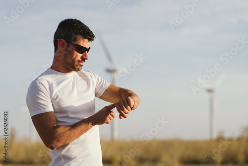 Male motivated athlete using sport watch for timing running workout. Man training outdoor.