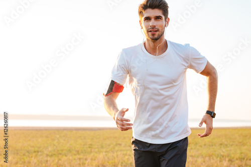 Handsome young sportsman running outdoors and listening to music