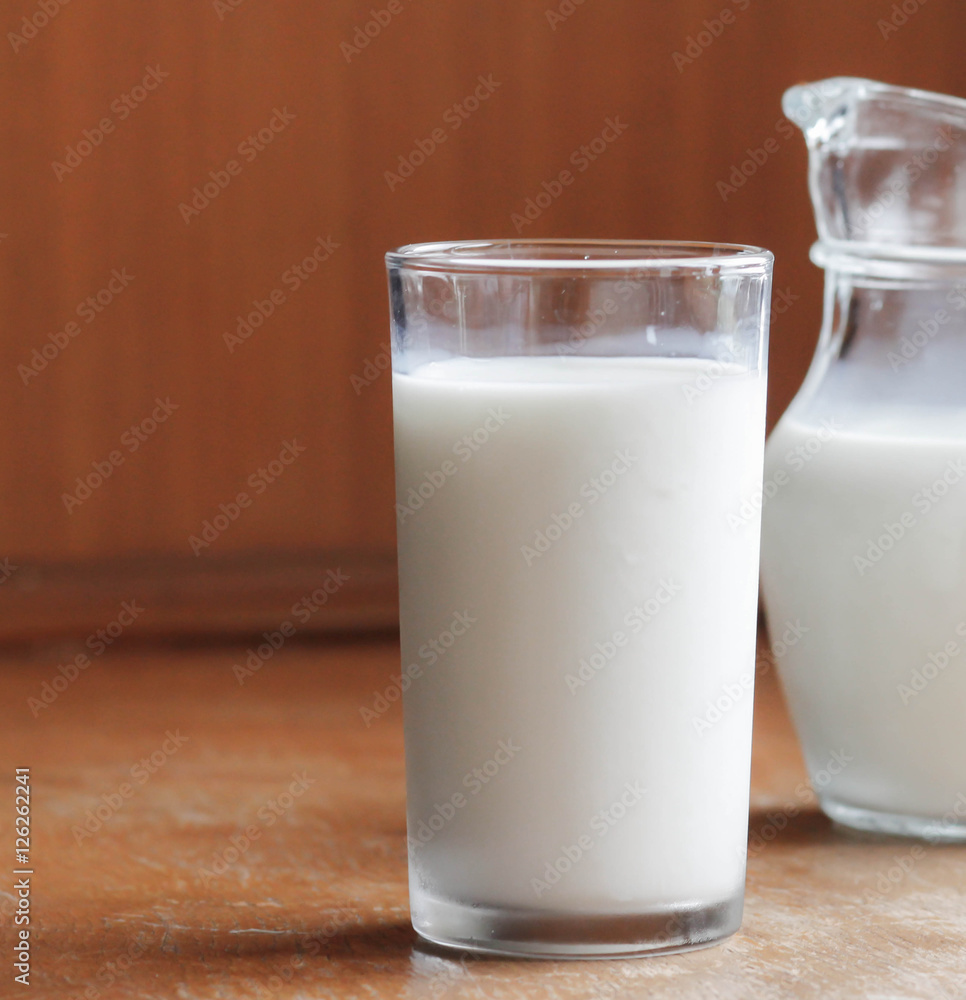 Natural whole milk in a jug and a glass on the old wooden background Natural whole milk in a jug and a glass on the old wooden background