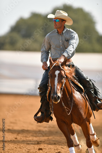 The front view of a rider in cowboy chaps, boots and hat on a horseback performs an exercise during a competition © PROMA