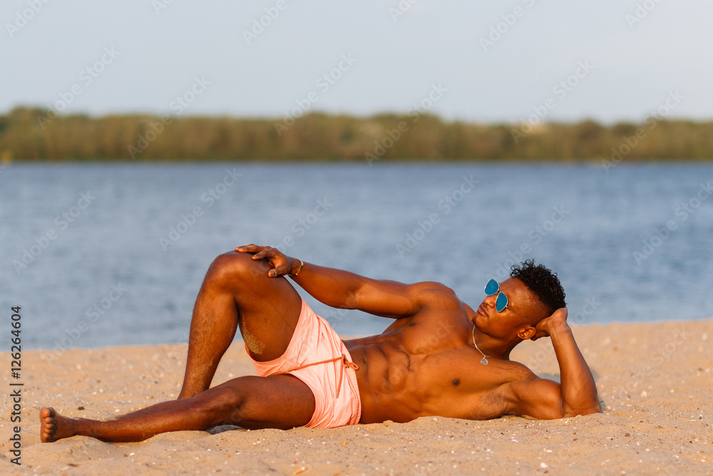 Fotografia do Stock: Muscular young athletic sexy man on the beach with a  naked torso in underwear. Hot black beautiful guy, fitness model with a  rangy sports body.