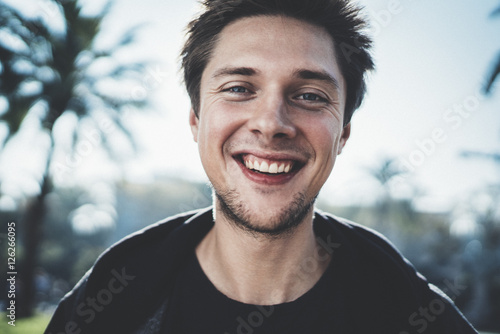 Close-up portrait of young happy smiling hipster guy looking at camera outdoor photo