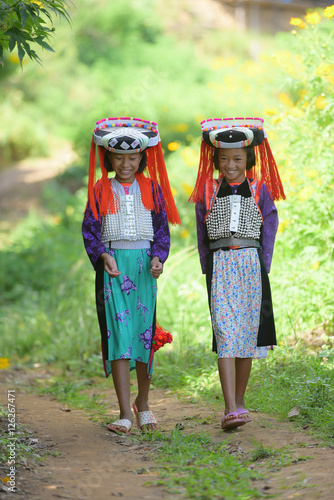 Two beautiful asian young Lahu tribe girls in custom dress walk in village with smile and happy. photo