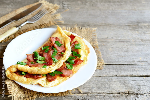 Fried egg omelet. Tasty omelet with fried bacon and fresh parsley on a plate, fork, knife on old wooden background with copy space for text. Delicious breakfast menu. Rustic style 
