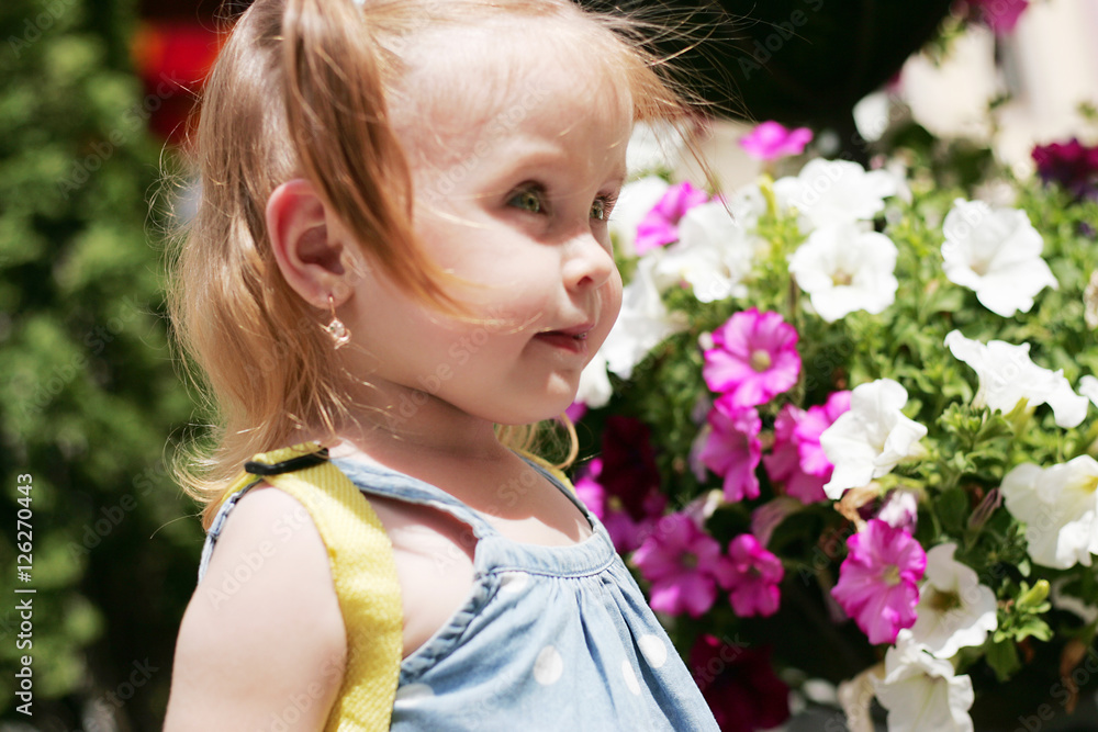 Fototapeta premium A little girl standing near flowers