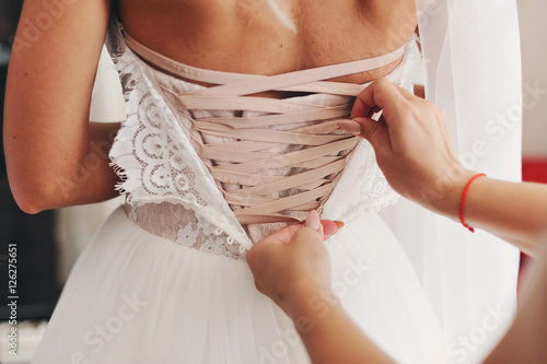 Руки девушки завязывают свадебное платье невесты