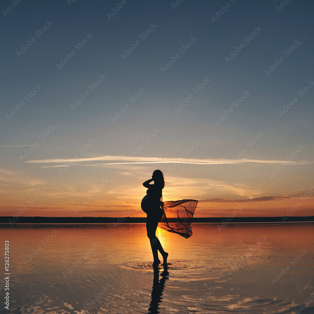 Силуэт беременной женщины в море на закате