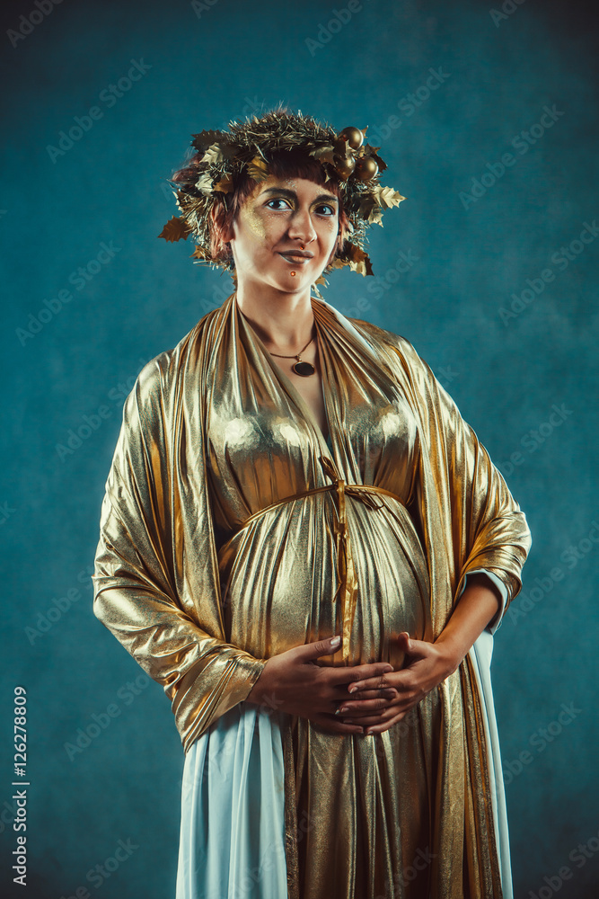 Pregnant woman in golden toga and wreath posing like a Greece fertility