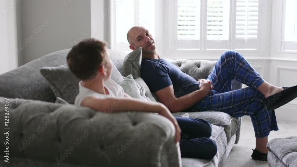 Father and son chatting together. They are sitting on the sofa in their living room. Father and son chatting together. They are sitting on the sofa in their living room.