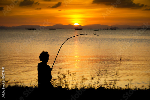 silhouette of fishermen with sunset sky on the lake.