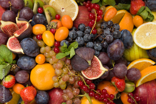 Fototapeta Naklejka Na Ścianę i Meble -  Top view on mixture of different fruit and berries: lemons, figs, grapes, tangerines, apples, strawberry, plums, red current, oranges. Healthy food concept