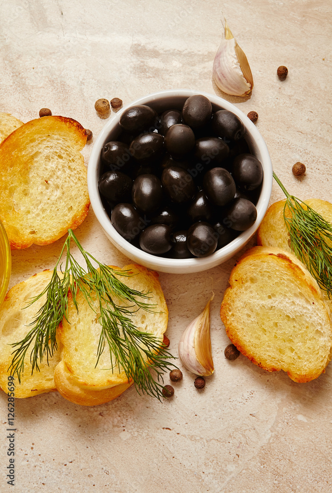 Italian food ingredients background with Ciabatta bread toasts, olive oil, black olives and garlic, spices on marble stone. 