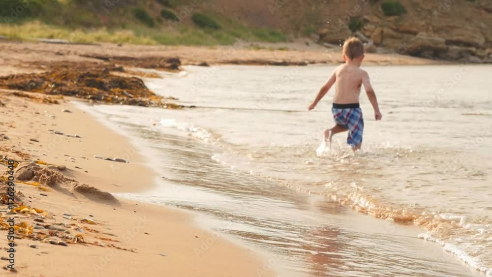 Slow motion shot of a boy running through ocean on beach