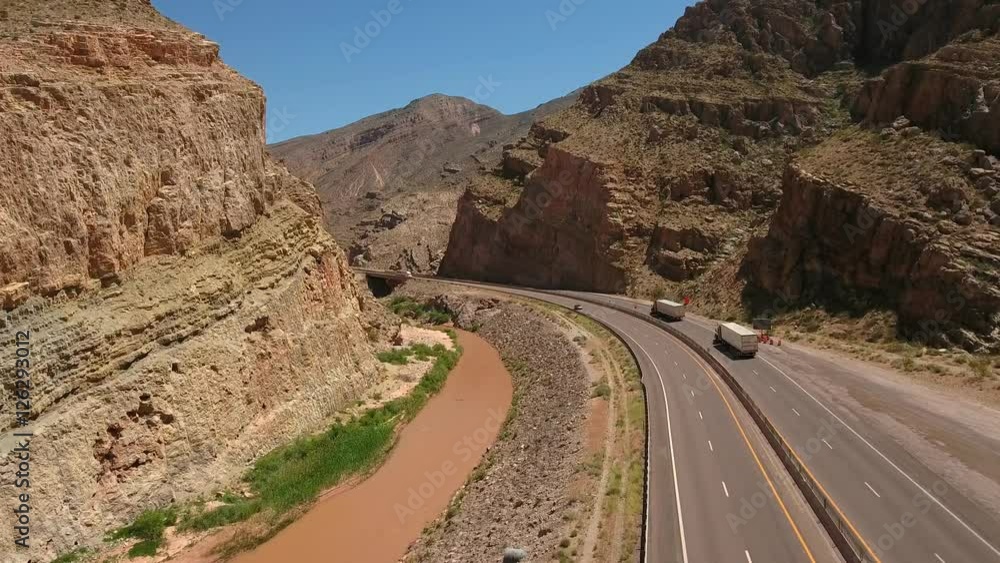Aerial shot of cars drive through desert canyon next to river Aerial shot of cars drive through desert canyon next to river