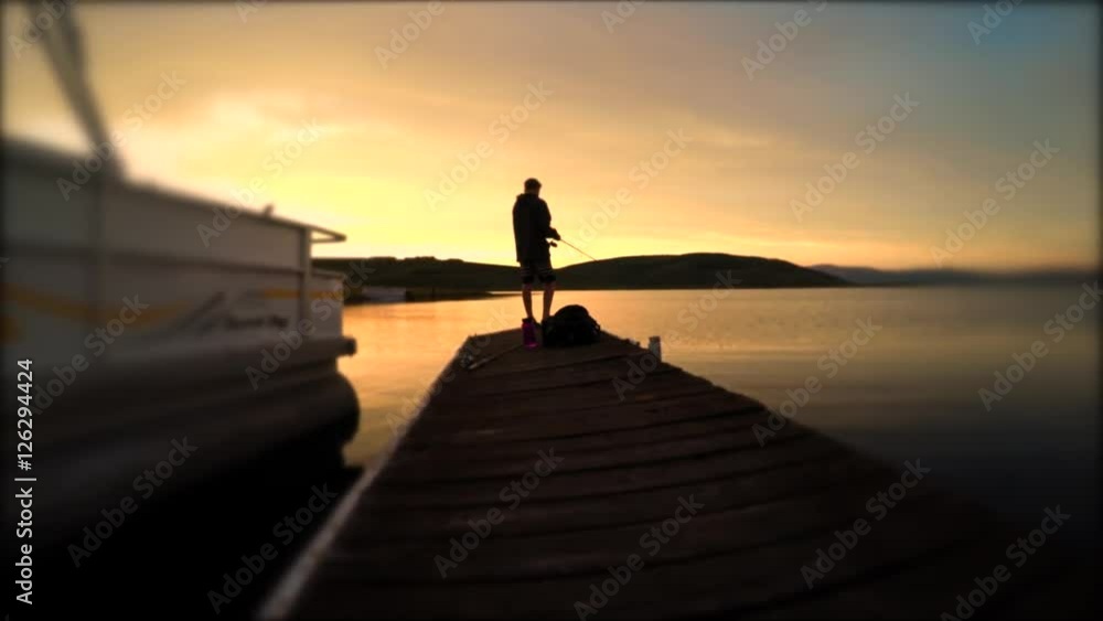 A teen fishing with a pole off a dock at sunset A teen fishing with a pole off a dock at sunset