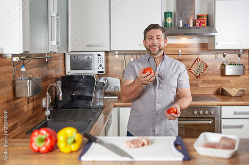 Man juggling with tomatoes in his kitchen laughing