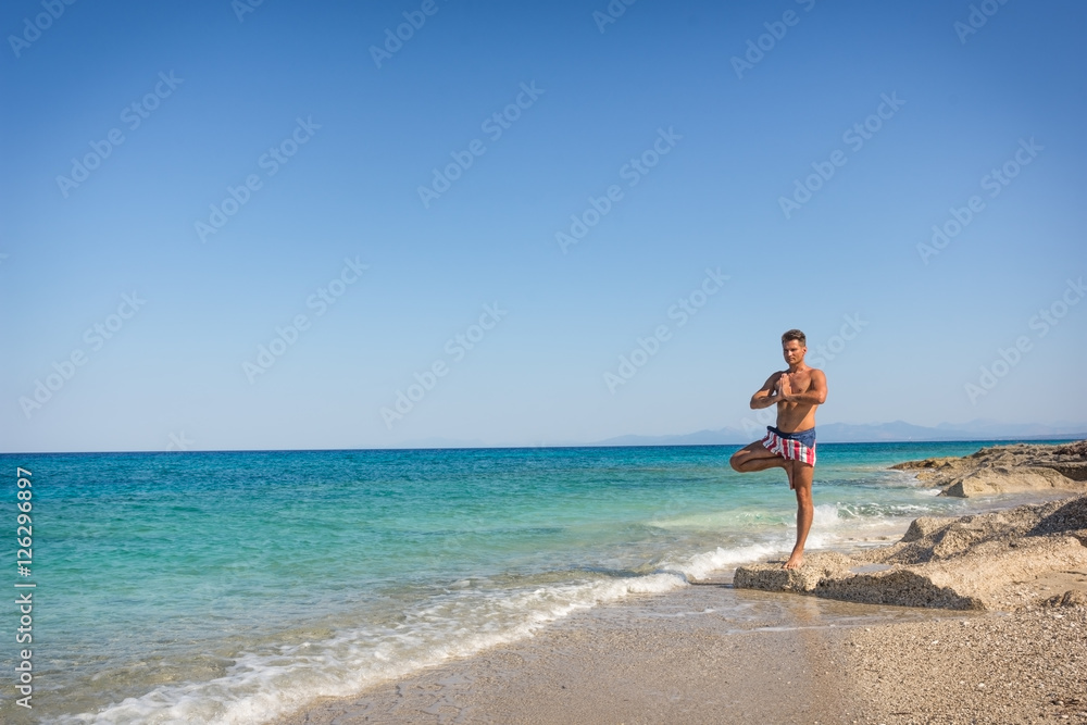 Adult man in yoga position, tree pose, on the waterfront, in Gre