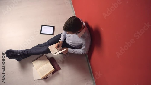 Young student man studying sitting on the floor near books and tablet pc photo