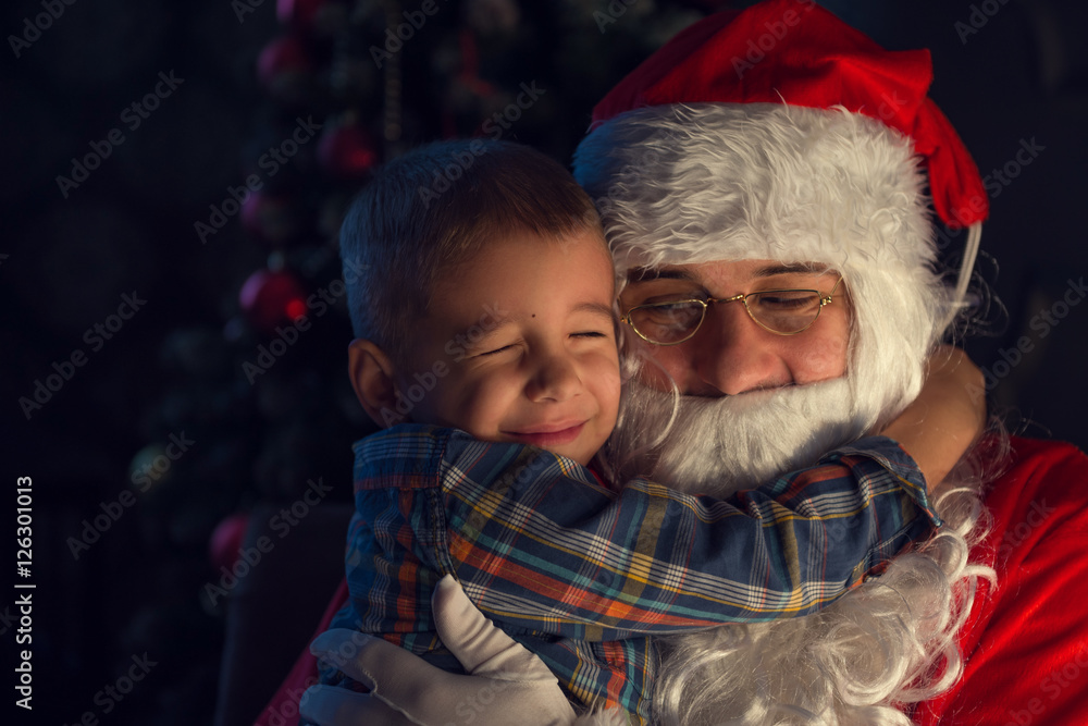 Portrait of a happy child with Santa Claus next to Christmas tree