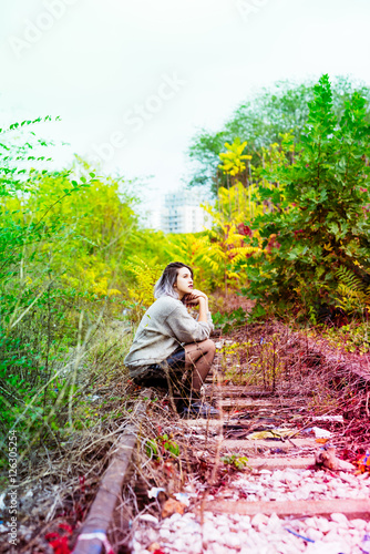 Young beautiful caucasian purple grey hair woman outdoor in the city sitting on abandoned railway, looking at camera - serious, pensive, thinking future concept