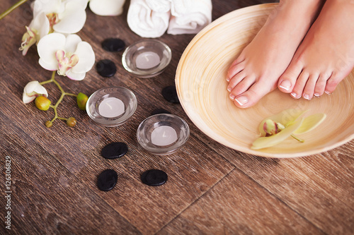 Female feet with drops of water, spa bowls, towels, flowers and candles.