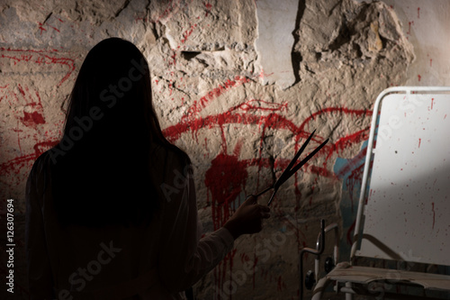 Fotografija Shadowy female figure holding blade near blood stained wall