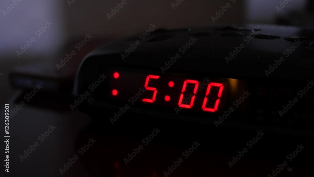 A digital alarm turns five and man turns off alarm