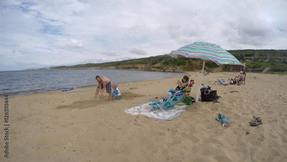 A timelapse shot of a man digging a hole in the sand with his toddler at the beach on the ocean A timelapse shot of a man digging a hole in the sand with his toddler at the beach on the ocean