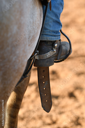 Western horseman leg in boot at stirrup on horse during the riding