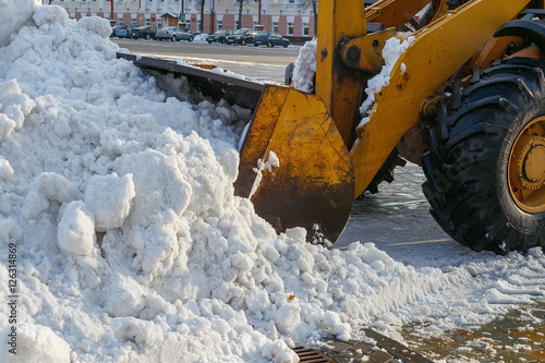 Snow removal equipment works in the city. Snow removal after a snowfall. Orange tractor with bucket loads of snow. Outdoors.