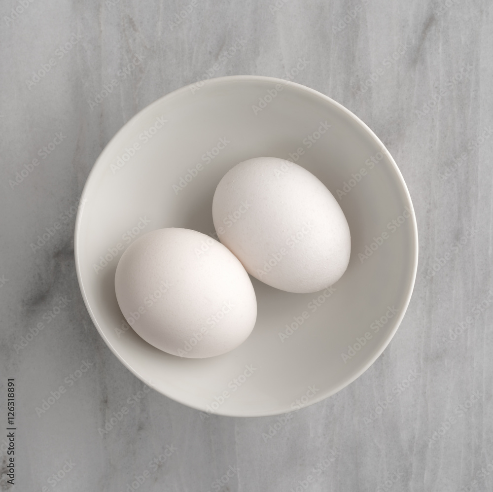Two eggs in a bowl atop a gray marble cutting board. Two eggs in a bowl atop a gray marble cutting board.