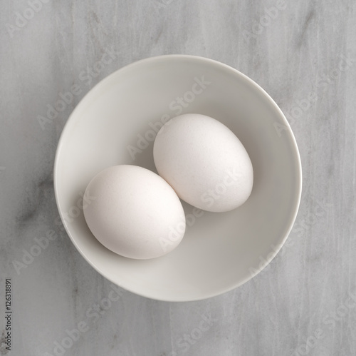 Two eggs in a bowl atop a gray marble cutting board.