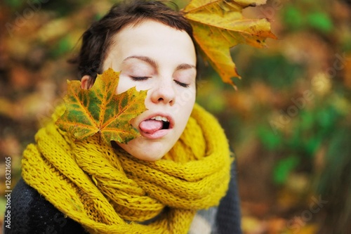 Young teen girl in a knitted scarf with maple leaves in her hair grimaces, showing tongue.