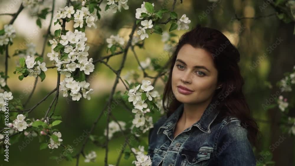 Young pretty smiling caucasian woman in jeans jacket standing near blooming spring tree. Youth, freshness, beauty, happiness concept. Young pretty smiling caucasian woman in jeans jacket standing near blooming spring tree. Youth, freshness, beauty, happiness concept.