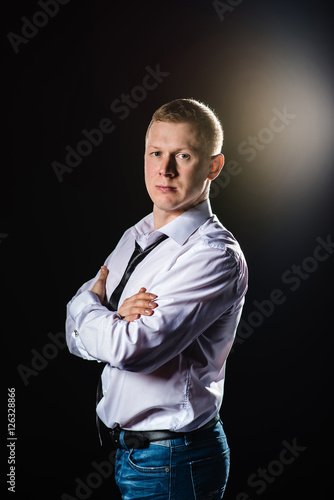 Serious man standing sides in a half-turn with folded hands. Studio shot flare at background.