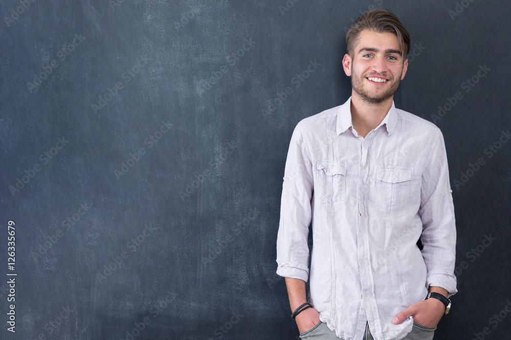 Handsome young student in shirt standing against blackboard