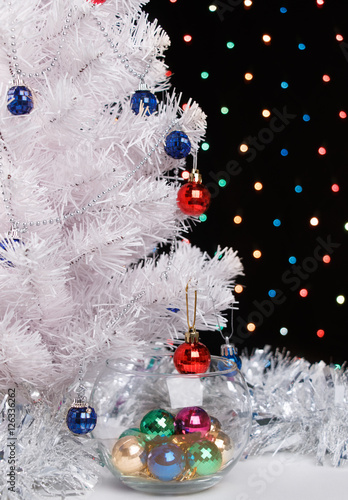 christmas balls in glass vase near by white fir-tree