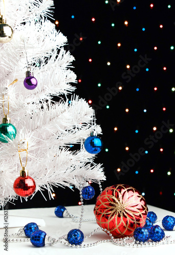 Red xmas ball near by decorated white fir-tree