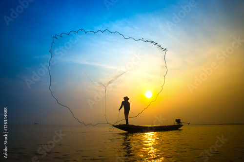 Silhouettes fisherman throwing fishing nets during sunset.