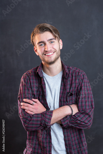 Happy young man standing with arms crossed over blackboard backg