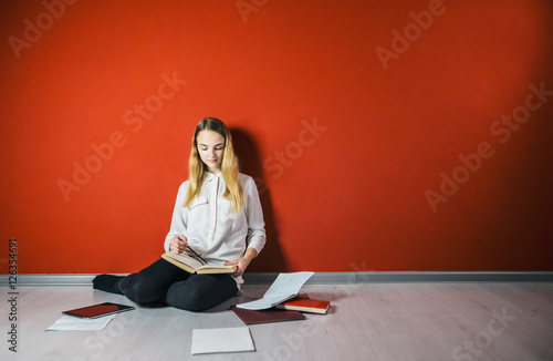 Young student girl studying sitting on the floor near books and tablet pc