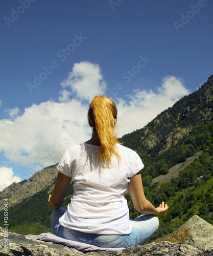 Young woman meditating on top of a mountain in the wilderness