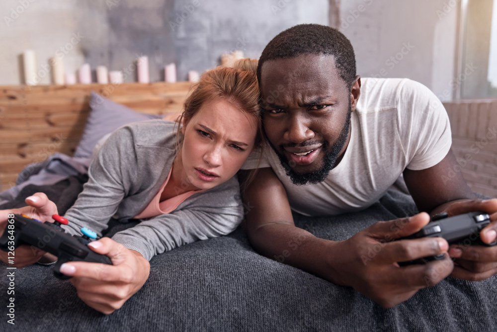 Fototapeta premium Amused couple playing video games in bedroom together