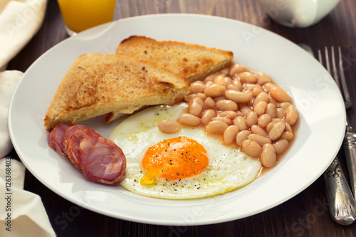 fried egg with chorizo, toast and beans on white plate