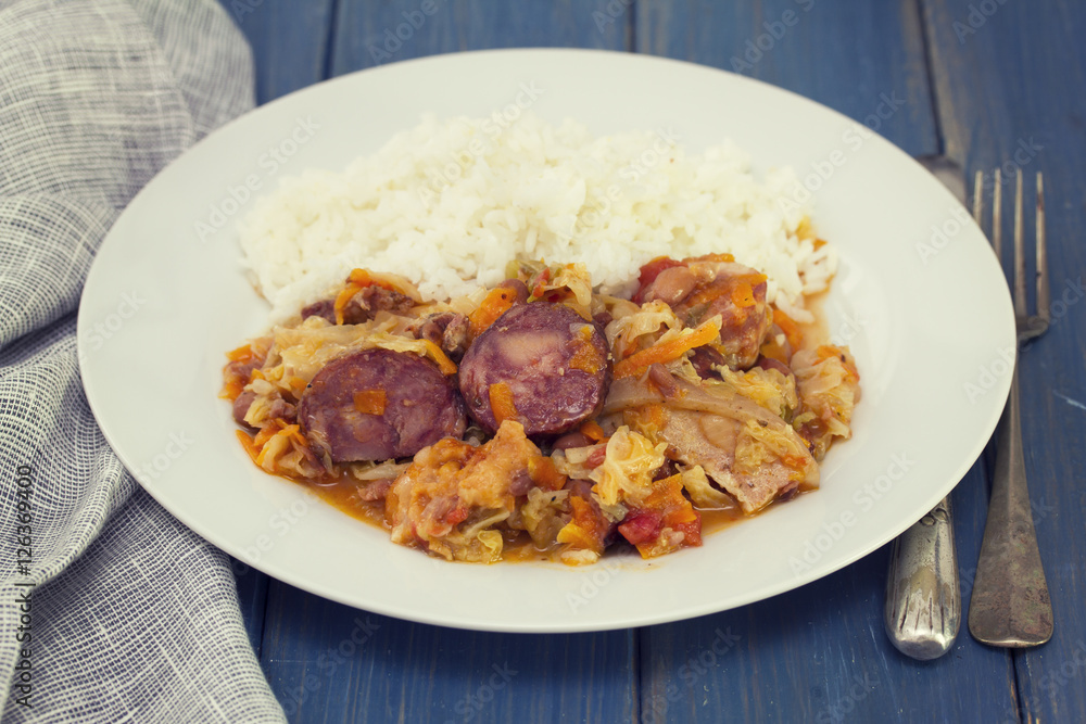 meat with sausages, cabbage and rice on white plate on wooden background