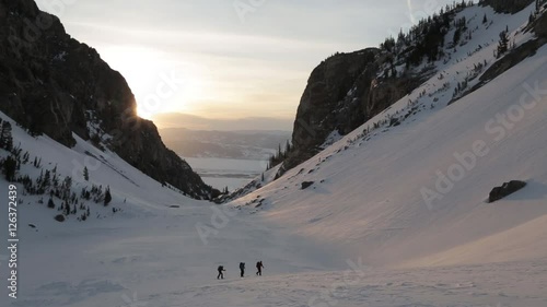 Skiers hiking or trekking across winter snowy mountain valley at sunset