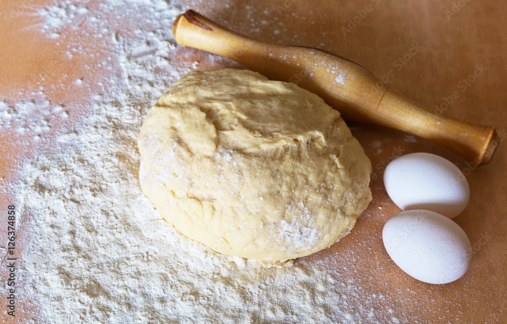 The kitchen table and preparation of yeast pastry. Flour, eggs and rolling pin The kitchen table and preparation of yeast pastry. Flour, eggs and rolling pin