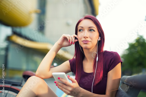 Red-haired girl sitting on the bench and use the phone