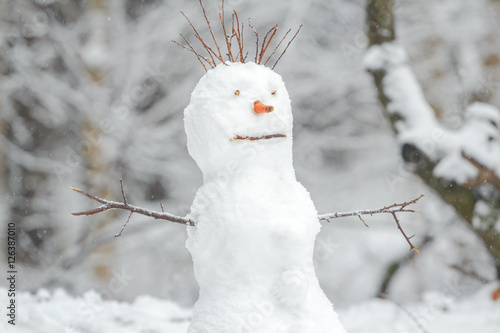 Snowy white snowman with carrot nose in winter Christmas outdoor background