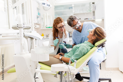 A young woman, seated in the dentist's chair, prepares herself for treatment, her trust in capable hands. Meanwhile, a two dentists discusses her care to ensure a seamless and comfortable experience.